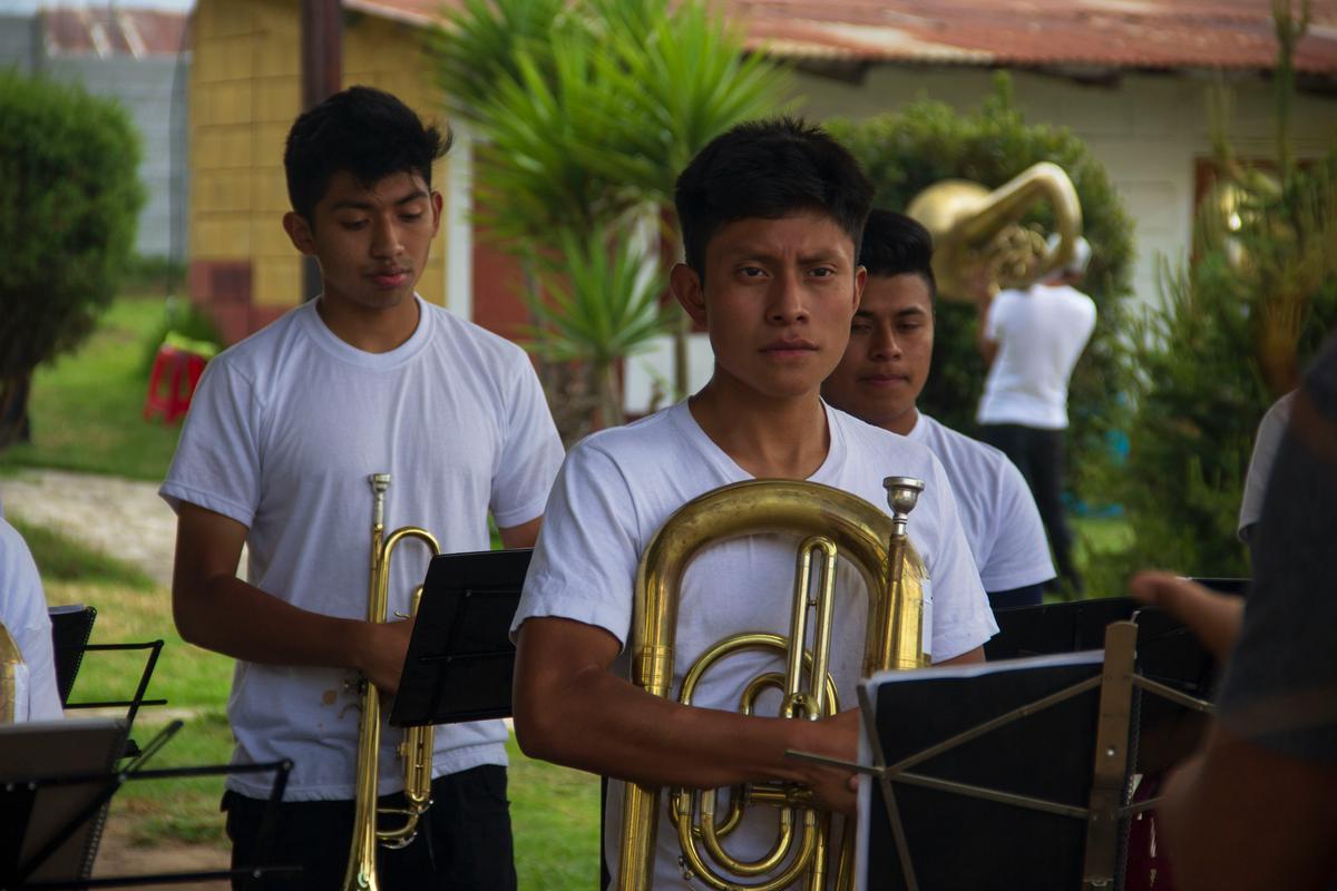 Una imagen de músicos tocando instrumentos típicos mexicanos en un escenario con luces de colores y bailarines alrededor